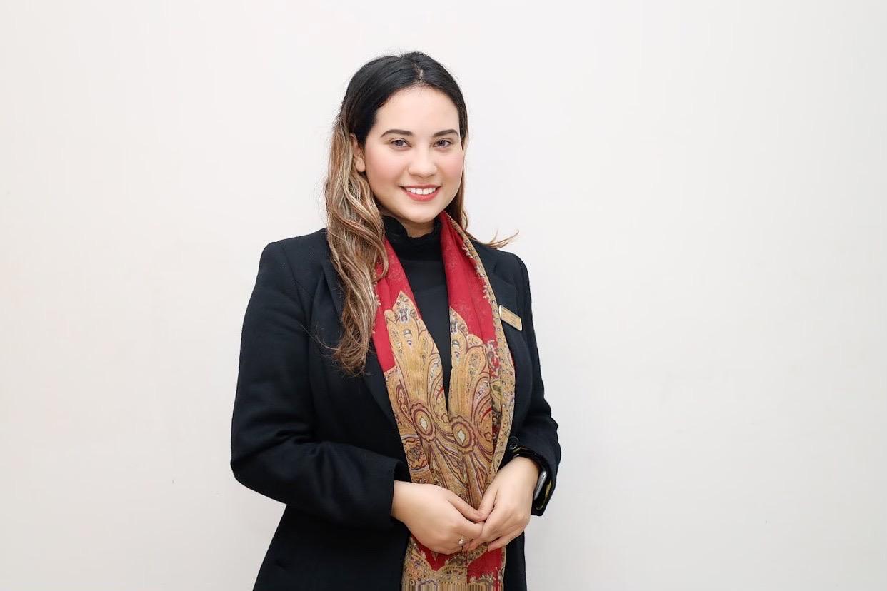 Smiling woman wearing a black blazer and a red patterned scarf against a white background